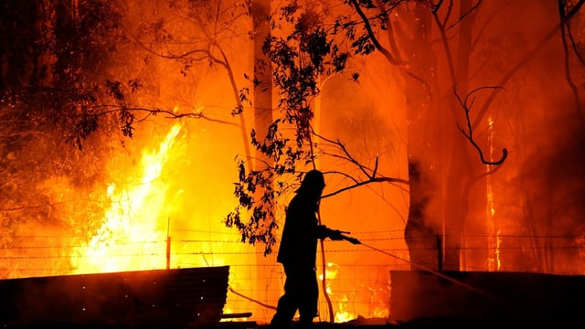 Ein Mann in Feuerschutzanzug vor einem Feuer bei Nacht. Ein Mann in Feuerschutzanzug vor einem Feuer bei Nacht.