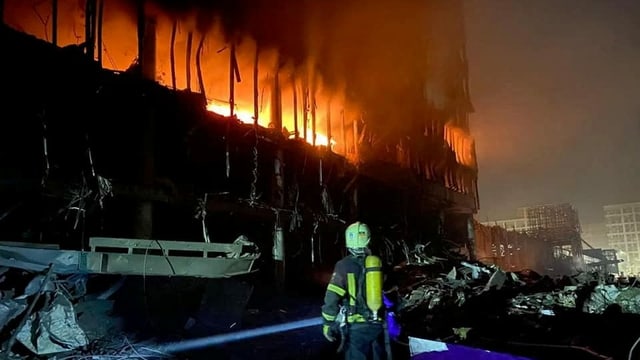 Ein Feuerwehrmann steht vor einem brennenden Gebäude.