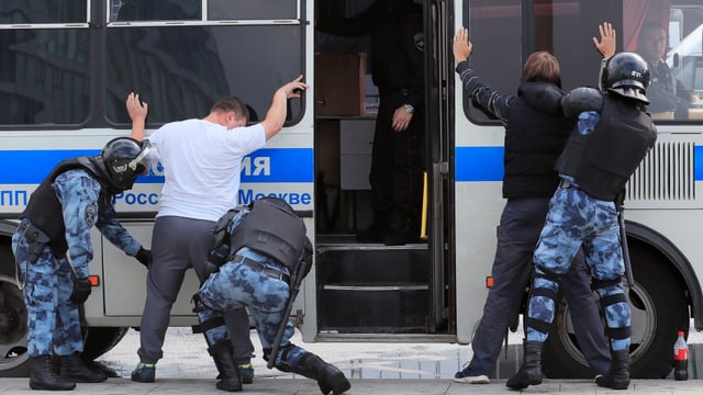 Polizeibus. Davor werden Personen von Polizisten durchsucht. Sie stehen mit erhobenen Armen und gespreizten Beinen vor dem Bus. Polizeibus. Davor werden Personen von Polizisten durchsucht. Sie stehen mit erhobenen Armen und gespreizten Beinen vor dem Bus.