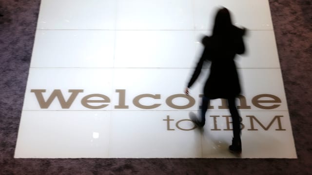 Die Silhouette einer Frau, die über ein IBM-Logo am Boden schreitet. Die Silhouette einer Frau, die über ein IBM-Logo am Boden schreitet.