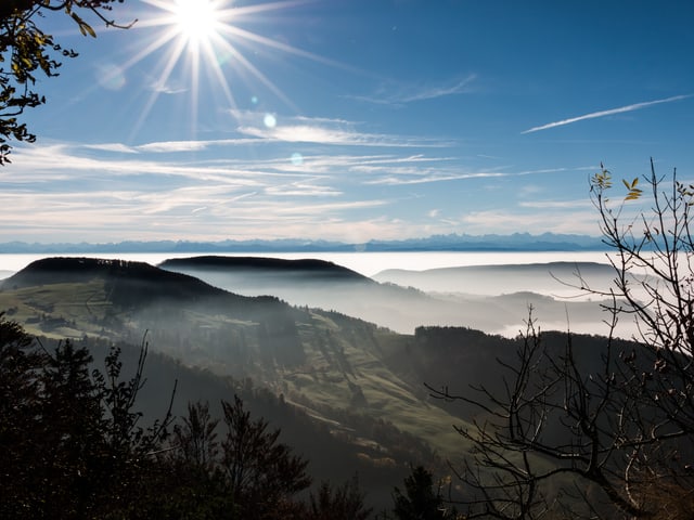 Vom Cellenchöpfli in Baselland ein Blick zu den Alpen. Im Vordergrund zeigen sich am Hauberg Dunst- und Nebelschleier, darüber ist der Himmel mit ein paar dünnen Wolken bedeckt, die Sonne scheint. Vom Cellenchöpfli in Baselland ein Blick zu den Alpen. Im Vordergrund zeigen sich am Hauberg Dunst- und Nebelschleier, darüber ist der Himmel mit ein paar dünnen Wolken bedeckt, die Sonne scheint.