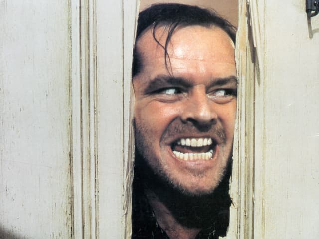Jack Nicholson steckt als Charakter Jack Torrance den Kopf durch ein Loch in der Tür und grinst diablolisch. Jack Nicholson steckt als Charakter Jack Torrance den Kopf durch ein Loch in der Tür und grinst diablolisch.