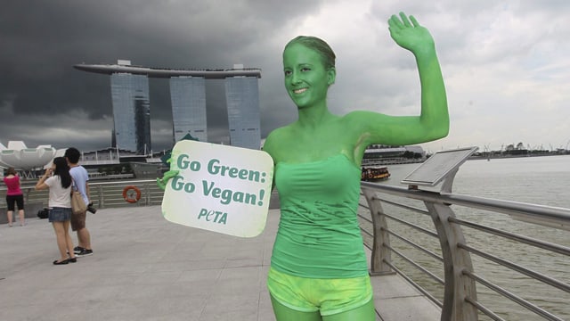 Frau in grünem Bodypainting mit Schild in der Hand: Go Green! Go Vegan!