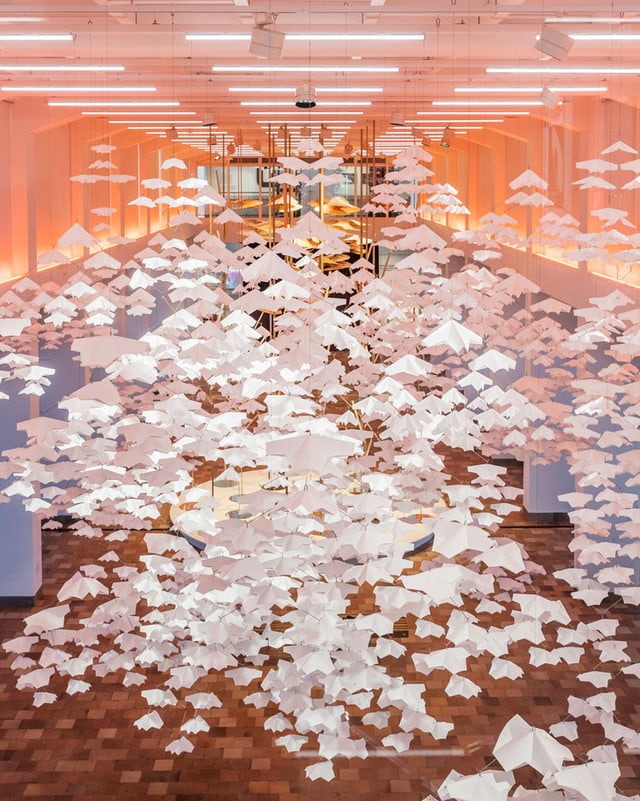 Ein Ausstellungsraum, in dem gefaltete Papiere von der Decke hängen. Ein Ausstellungsraum, in dem gefaltete Papiere von der Decke hängen.