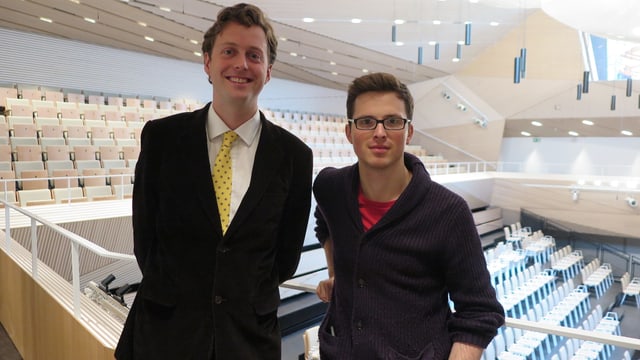 Zwei junge Männer stehen in der hellen neuen Konzerthalle. Zwei junge Männer stehen in der hellen neuen Konzerthalle.