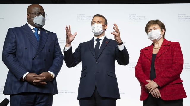 Die drei Personen stehen nebeneinander, Macron in der Mitte gestikuliert. Die drei Personen stehen nebeneinander, Macron in der Mitte gestikuliert.