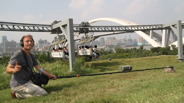 Ein Mann mit einem Stangenmikrophon vor einer Sesselbahn in Shanghai. Ein Mann mit einem Stangenmikrophon vor einer Sesselbahn in Shanghai.