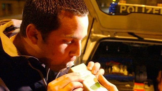 Ein Mann bläst anlässlich einer nächtlichen Polizeikontrolle in ein Atemtestgerät, daneben der Polizeibeamte. Ein Mann bläst anlässlich einer nächtlichen Polizeikontrolle in ein Atemtestgerät, daneben der Polizeibeamte.