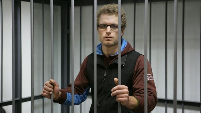 Marco Weber ist in einem Käfig eingesperrt. Er hat die Hände an den Gitterstäben und blickt in die Kamera. Marco Weber ist in einem Käfig eingesperrt. Er hat die Hände an den Gitterstäben und blickt in die Kamera.