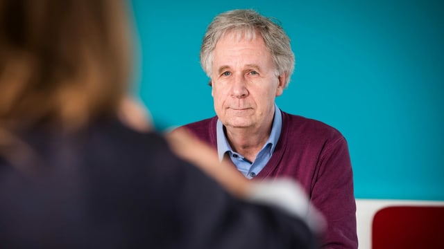 Ein älterer Mann mit weinrotem Pulli lächelt sein Gegenüber an. Ein älterer Mann mit weinrotem Pulli lächelt sein Gegenüber an.