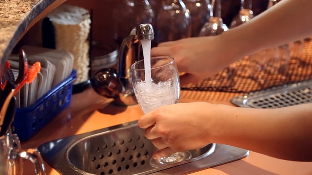 Man sieht Hände, die ein Glas unter den Wasserhahn halten. Man sieht Hände, die ein Glas unter den Wasserhahn halten.