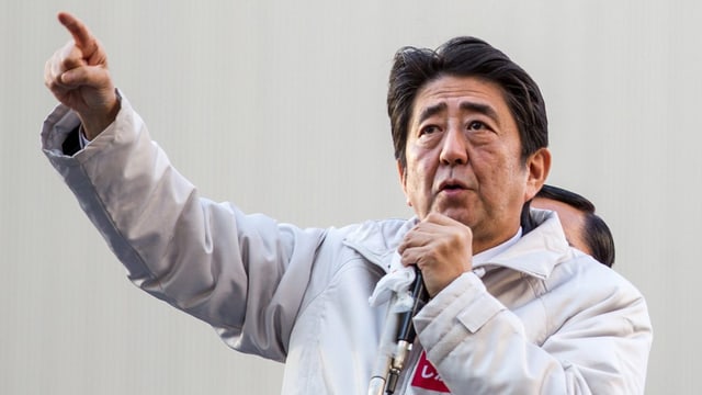 Shinzo Abe hält ein Mikrofon und hält den rechten Arm mit ausgestrecktem Zeigefinger hoch Shinzo Abe hält ein Mikrofon und hält den rechten Arm mit ausgestrecktem Zeigefinger hoch