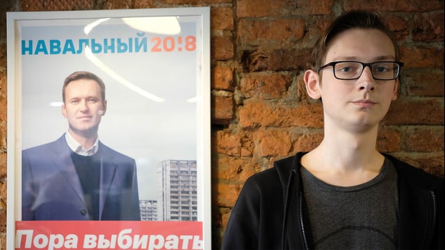 Andrei steht vor einem Navalny-Poster. Andrei steht vor einem Navalny-Poster.