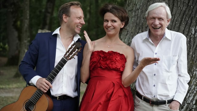 Rechts und links ein Mann, in der Mitte eine Frau. Der Mann rechts mit Gitarre in der Hand. Sie stehen vor einem Baum und strahlen. Rechts und links ein Mann, in der Mitte eine Frau. Der Mann rechts mit Gitarre in der Hand. Sie stehen vor einem Baum und strahlen.
