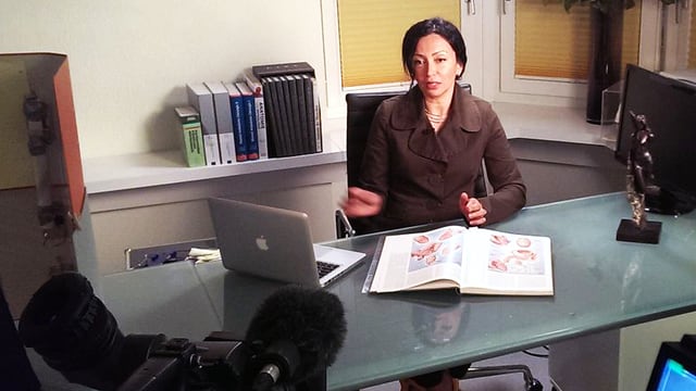 Eine Frau sitzt an einem Pult, vor sich hat sie einen Laptop und ein Buch mit medizinischen Illustrationen. Eine Frau sitzt an einem Pult, vor sich hat sie einen Laptop und ein Buch mit medizinischen Illustrationen.