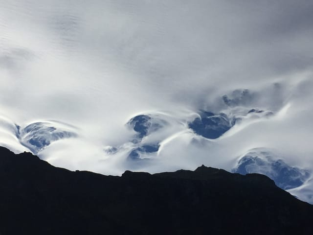 Unten schwarze Konturen der Berge, oben bedeckter Himmel. Am Horizont hat es Wirbel in der Wolkendecke.