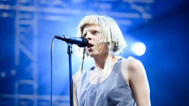 Blonde Musikerin singt in Mikrofon vor blauem Hintergurnd Blonde Musikerin singt in Mikrofon vor blauem Hintergurnd