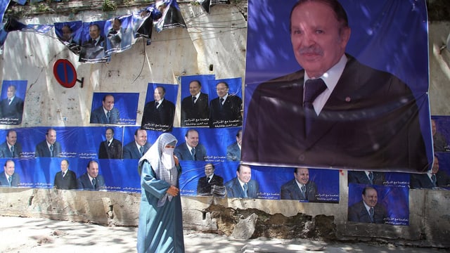 Eine Frau geht vor einer Mauer mit Wahlplakaten von Bouteflika. Eine Frau geht vor einer Mauer mit Wahlplakaten von Bouteflika.