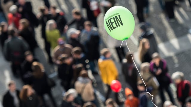Ein gelber Ballon mit dem Schriftzug «Nein» schwebt über einer Menschenmenge, Blick von oben. Ein gelber Ballon mit dem Schriftzug «Nein» schwebt über einer Menschenmenge, Blick von oben.