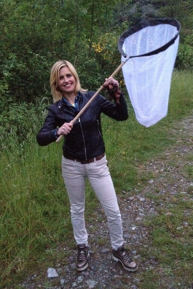 Frau steht mit einem grossen Schmetterlingsfangnetz auf einem Waldweg.
