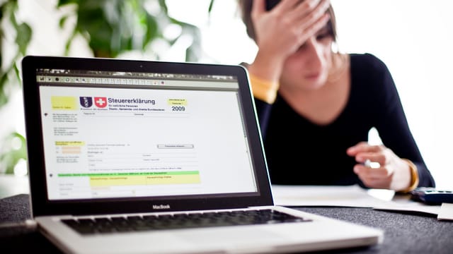 Laptop mit Steuererklärung auf dem Bildschirm, daneben Frau, die sich den Kopf hält Laptop mit Steuererklärung auf dem Bildschirm, daneben Frau, die sich den Kopf hält