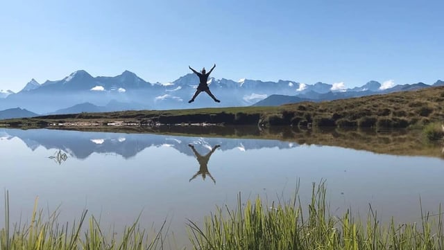 Eine Frau springt in die Luft vor Alpenpanorama. Davor ein See. Eine Frau springt in die Luft vor Alpenpanorama. Davor ein See.