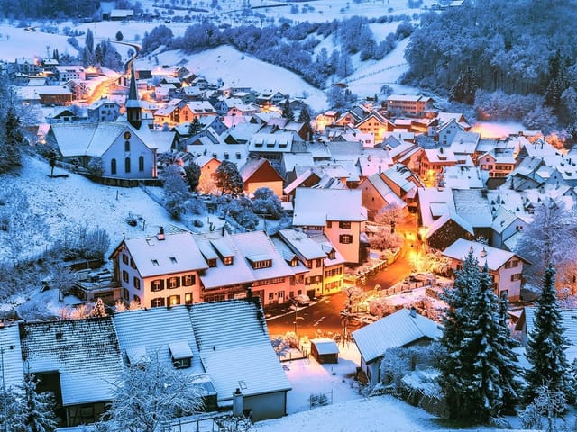 Dorf in der Dämmerung mit Neuschnee und Lichtern.