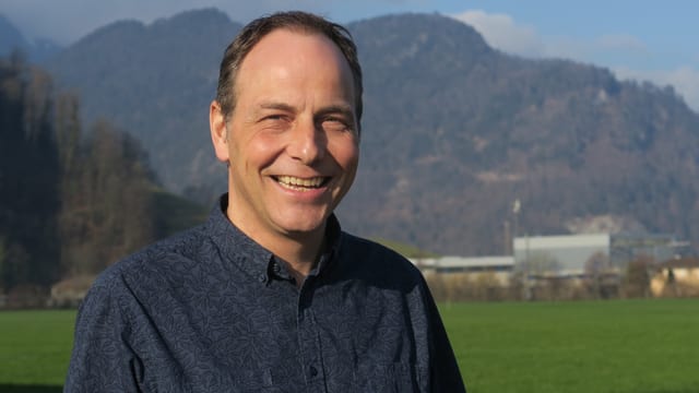 Ein Mann mit einem dunkelblauen Hemd steht auf einer Wiese und schaut in die Kamera. Ein Mann mit einem dunkelblauen Hemd steht auf einer Wiese und schaut in die Kamera.