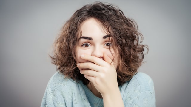 Eine junge Frau hält sich die Hand vor den Mund Eine junge Frau hält sich die Hand vor den Mund