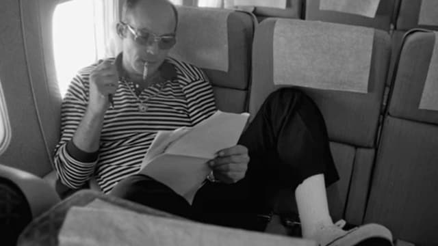 Ein Mann sitzt im Flugzeug, raucht und liest.