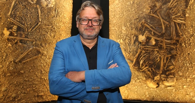 Ein Mann steht vor einem Bild eines archäologischen Fundes. Ein Mann steht vor einem Bild eines archäologischen Fundes.