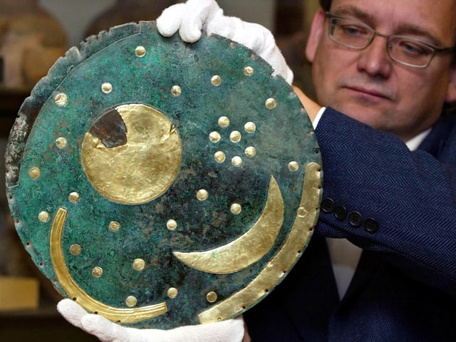 Ein Mann mit weissen Handschuhen hält eine türkisfarbene Scheibe mit goldener Sonne, Mond und Sterne Ein Mann mit weissen Handschuhen hält eine türkisfarbene Scheibe mit goldener Sonne, Mond und Sterne