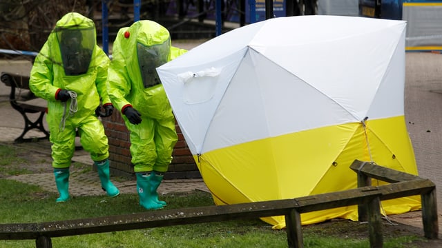 Zwei Polizisten in gelben Schutzanzügen nähern sich einem weiss-gelben Zelt. Zwei Polizisten in gelben Schutzanzügen nähern sich einem weiss-gelben Zelt.