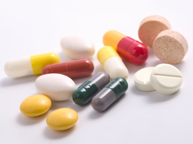 Auf einem Tisch liegen mehrere, verschiedene Pillen von Medikamenten in verschiedenen Farben.