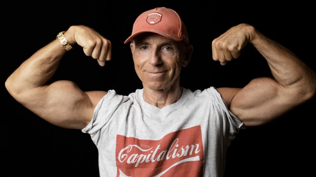 Mann mit vielen Cap und Muskelshirt steht da und zeigt seine muskelbepackten Oberarme. Er grinst zufrieden in die Kamera. Mann mit vielen Cap und Muskelshirt steht da und zeigt seine muskelbepackten Oberarme. Er grinst zufrieden in die Kamera.