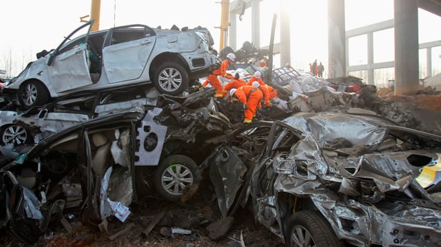 Autowracks sind aufeinander getürmt, Helfer klettern herum Autowracks sind aufeinander getürmt, Helfer klettern herum