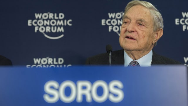Soros auf Rednertribüne mit Namensschild im Vordergrund. Soros auf Rednertribüne mit Namensschild im Vordergrund.
