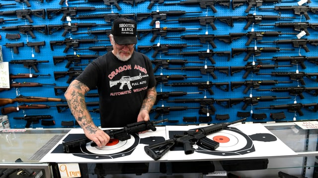 Ein Mann verkauft Waffen hinter einer Theke. Ein Mann verkauft Waffen hinter einer Theke.