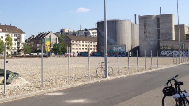 Man sieht einen Schotterplatz und im Hintergrund Wohnhäuser Man sieht einen Schotterplatz und im Hintergrund Wohnhäuser