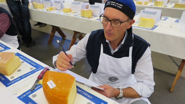 Ein Mann mit Brille, Bleistift und Block in den Händen, sitzt vor einem Käse. Ein Mann mit Brille, Bleistift und Block in den Händen, sitzt vor einem Käse.