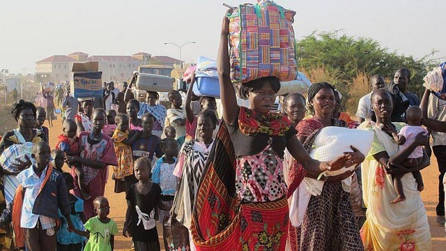 Eine Kolonne mit Südsudanesen, viele halten Gepäckstücke auf dem Kopf. Eine Kolonne mit Südsudanesen, viele halten Gepäckstücke auf dem Kopf.