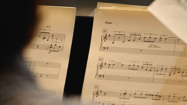 Eine Person vor einem Notenblatt sitzend.