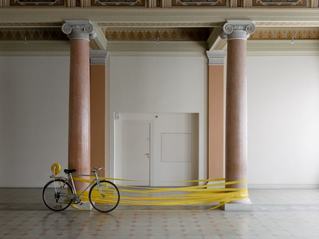 An zwei Säulen gelehnt steht ein Fahrrad, dahinter ist gelbes Band um die Säulen gewickelt. An zwei Säulen gelehnt steht ein Fahrrad, dahinter ist gelbes Band um die Säulen gewickelt.