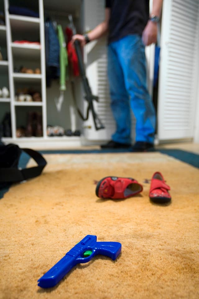 Ein Mann stellt sein Sturmgewehr in den Kleiderschrank, im Vordergrund liegen Kinderschuhe und eine Spielzeugpistole (2006). Ein Mann stellt sein Sturmgewehr in den Kleiderschrank, im Vordergrund liegen Kinderschuhe und eine Spielzeugpistole (2006).