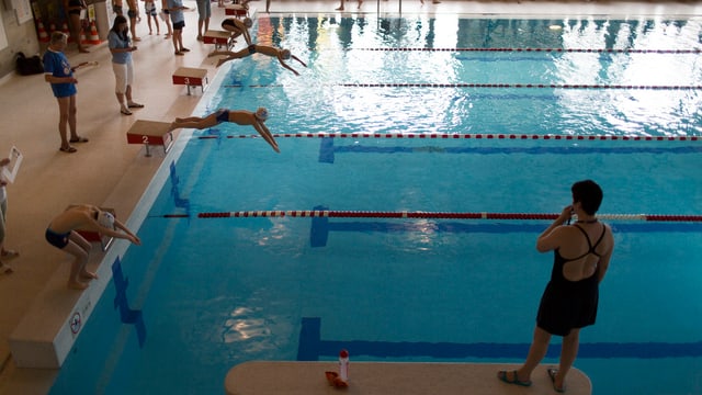 Kinder springen ins Schwimmbassin unter Aufsicht einer Schwimmlehrerin Kinder springen ins Schwimmbassin unter Aufsicht einer Schwimmlehrerin