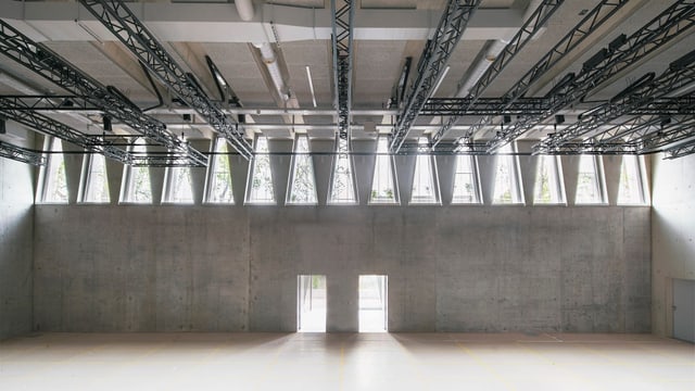Innenansicht des Tanzhauses: Sichtbeton, zwei Türen und dreieckige Fenster, durch die Licht fällt. Innenansicht des Tanzhauses: Sichtbeton, zwei Türen und dreieckige Fenster, durch die Licht fällt.
