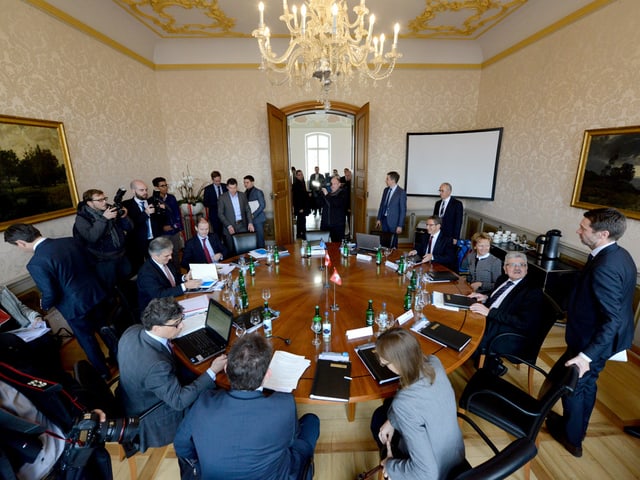 Runder Tisch in einem Sitzungszimmer im Regierungsgebäude voll mit Leuten Runder Tisch in einem Sitzungszimmer im Regierungsgebäude voll mit Leuten