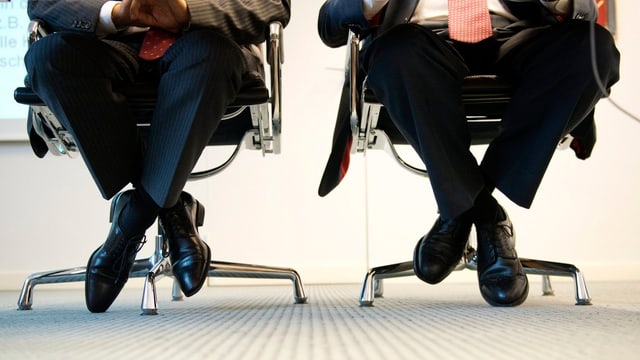 Zwei Männer in Anzügen sitzen auf Bürostühlen. Zwei Männer in Anzügen sitzen auf Bürostühlen.