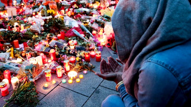 Eine junge Frau sitzt mit Kapuzze und gefalteten Händen nach dem Amoklauf in München vor Kerzen und Blumen. Eine junge Frau sitzt mit Kapuzze und gefalteten Händen nach dem Amoklauf in München vor Kerzen und Blumen.