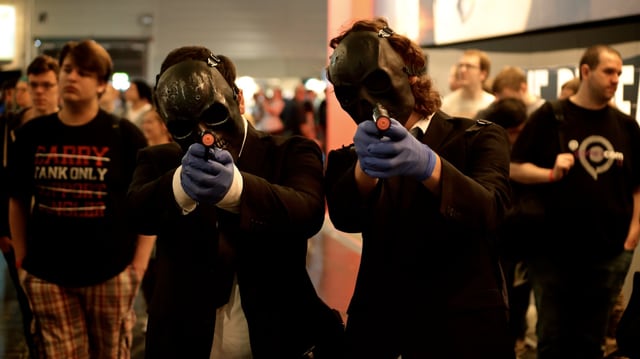 Zwei Männer in schwarzen Totenkopf-Masken und Gummihandschuhen ziehen ihre Pistolen.